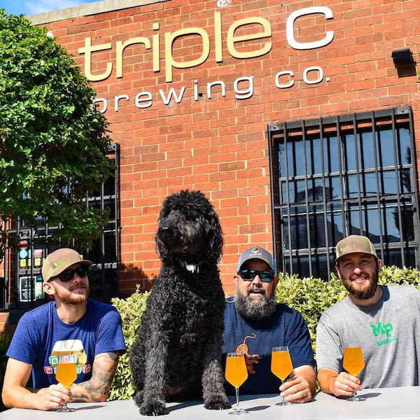black labradoodle dog sitting with three men drinking beer outside triple c brewing in south end charlotte, n.c.